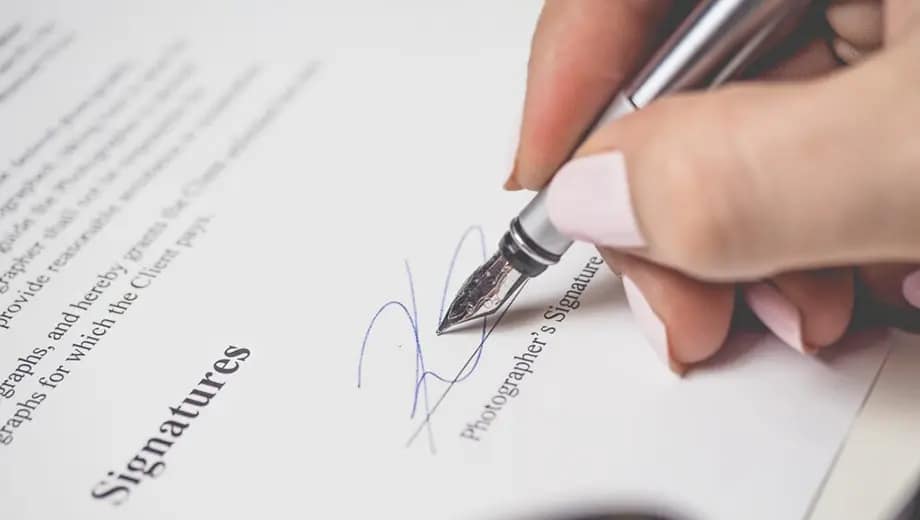 La imagen muestra a una mano firmando un documento.